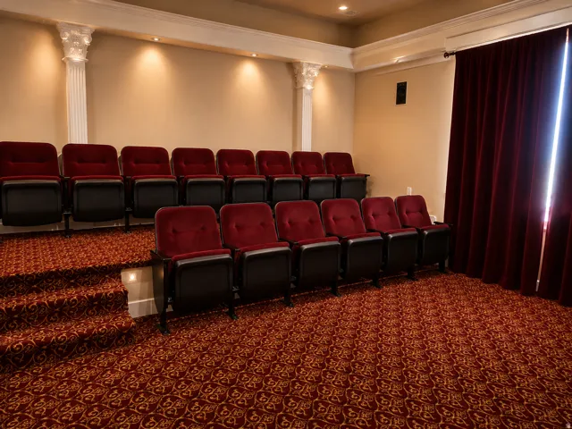 Tiered seating with upholstered chairs, ornate patterned carpet, decorative architectural columns, and recessed lighting