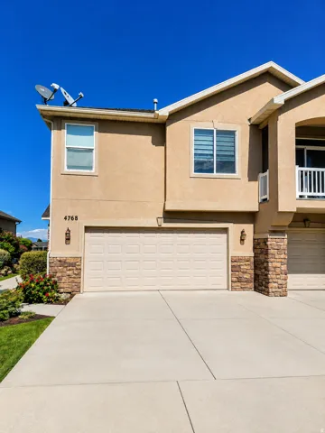 Stucco exterior with stone accents, an attached garage, a concrete driveway, and exterior lighting fixtures