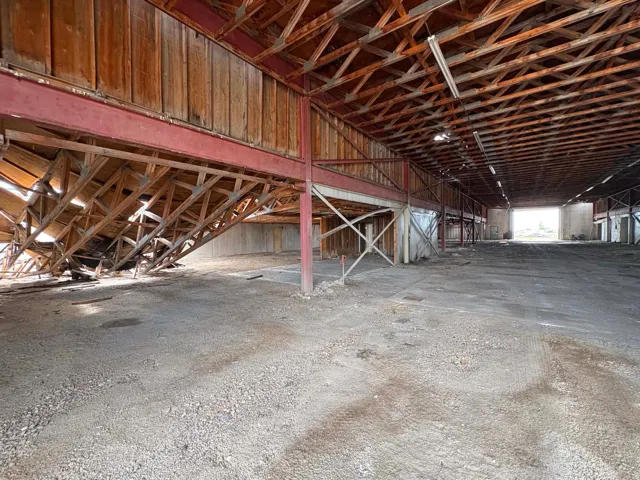 Exposed wood beam ceiling, expansive concrete flooring, visible structural support beams, and a high-clearance entryway