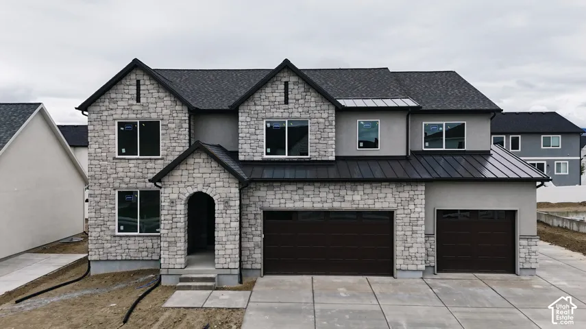 Two-story exterior featuring multi-textured stone masonry, smooth stucco siding, metal roof accents, a multi-car garage, and an arched entryway