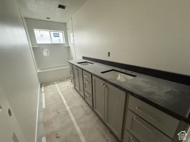 Dual-sink vanity featuring neutral-toned cabinetry, dark solid-surface countertops, and rectangular under-mount sinks, paired with a shower-tub combination featuring built-in shelving