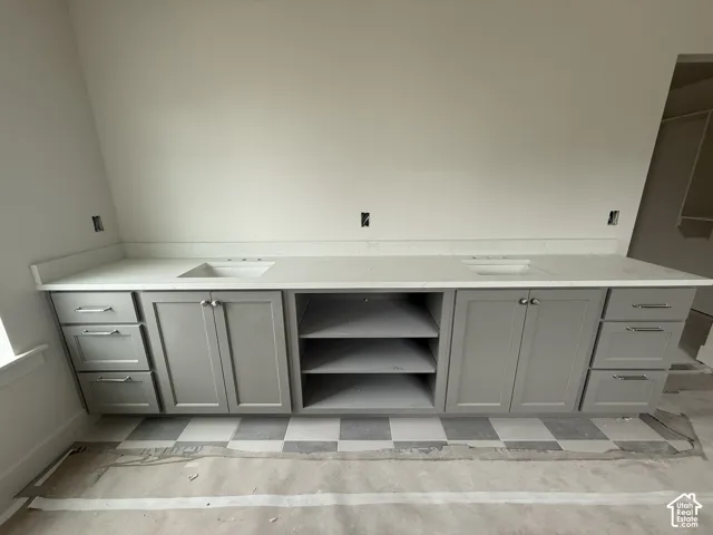 Double vanity featuring grey shaker-style cabinetry, white solid-surface countertops, dual integrated sinks, and open center shelving