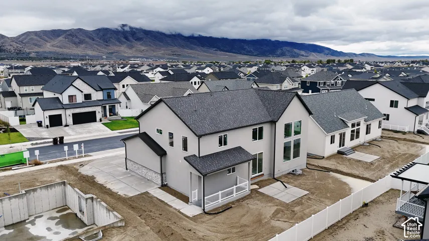 Two-story stucco and stone exterior featuring a gabled roof, concrete patio, white vinyl fencing, and mountain backdrop