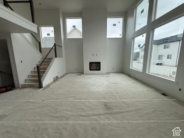 Double-height living area featuring a central fireplace, floor-to-ceiling windows, and a staircase with open railing