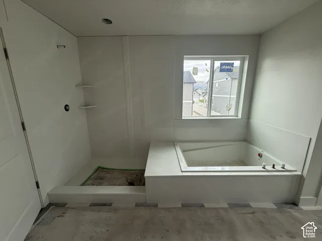 Soaking tub with a wide deck, integrated walk-in shower surround, built-in shelving, and a large window
