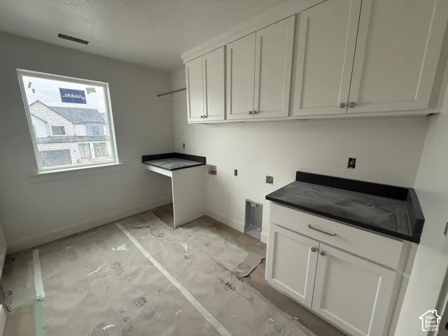 Laundry space featuring white shaker-style cabinetry, dark stone-finish countertops, and a built-in folding station
