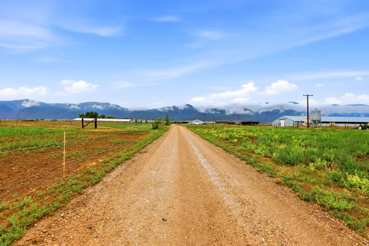 Expansive rural property featuring a gravel road, distant mountains, and agricultural structures