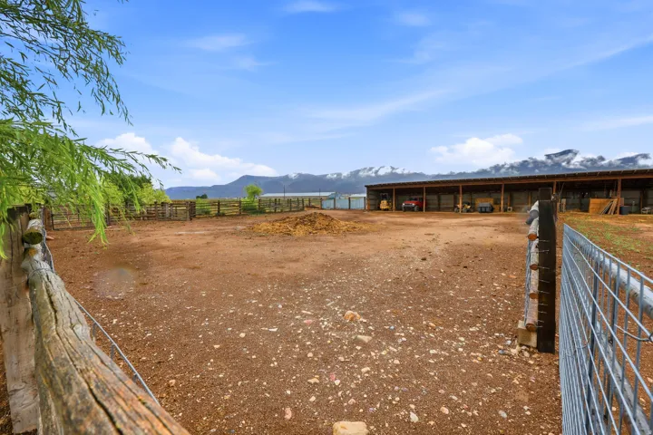 Expansive open-air barn with multiple bays, wood fencing, and metal gate