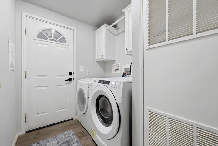 White utility room featuring wood-finish flooring, overhead cabinetry, and a white paneled door with an arched window