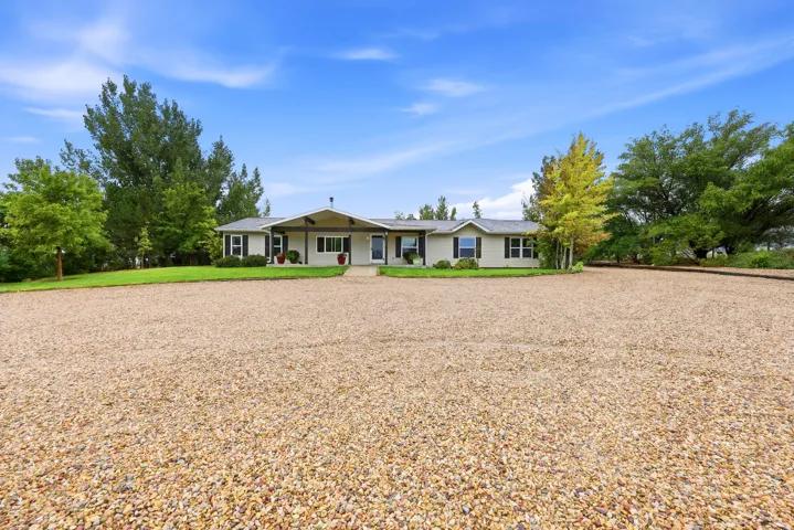 Expansive gravel driveway, manicured lawn, mature trees, and a single-story residence with a covered entry