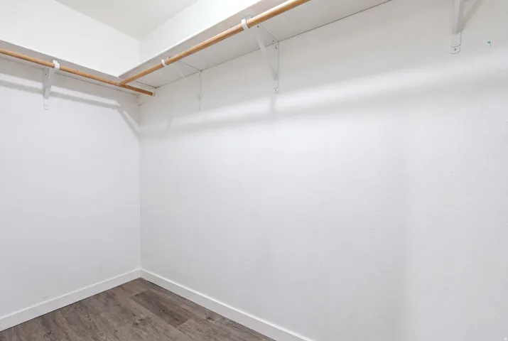 Walk-in closet featuring white walls, wood-finish flooring, and two wood rods with white support brackets