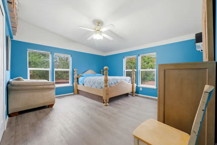 Vaulted ceiling with a ceiling fan, two windows, and wood-finish flooring