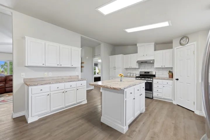 Modern kitchen featuring white cabinetry, light-toned countertops, a central island, stainless steel appliances, and wood-finish flooring