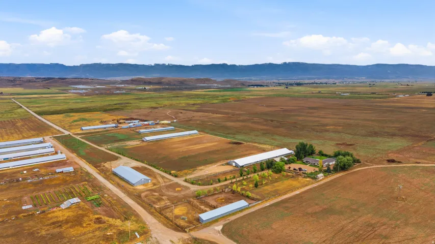 Expansive agricultural property featuring multiple outbuildings, structured fields, and a distant mountain backdrop