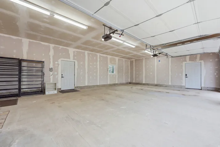 Spacious garage with multiple entry doors, exposed drywall, and overhead fluorescent lighting