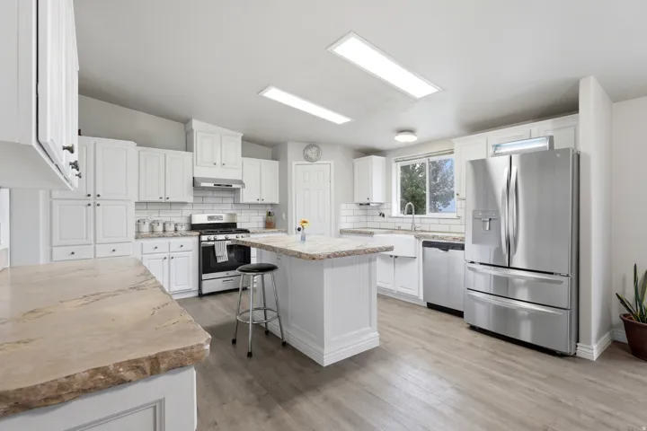 Kitchen featuring white cabinetry, wood-finish flooring, stainless steel appliances, a center island with bar seating, and light-toned countertops