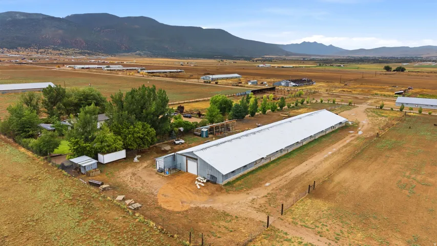 Expansive property featuring multiple outbuildings, agricultural structures, a metal roof building, and surrounding acreage with distant mountain ranges