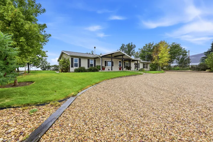 Ranch-style residence featuring a gravel driveway, covered entry, and black window shutters