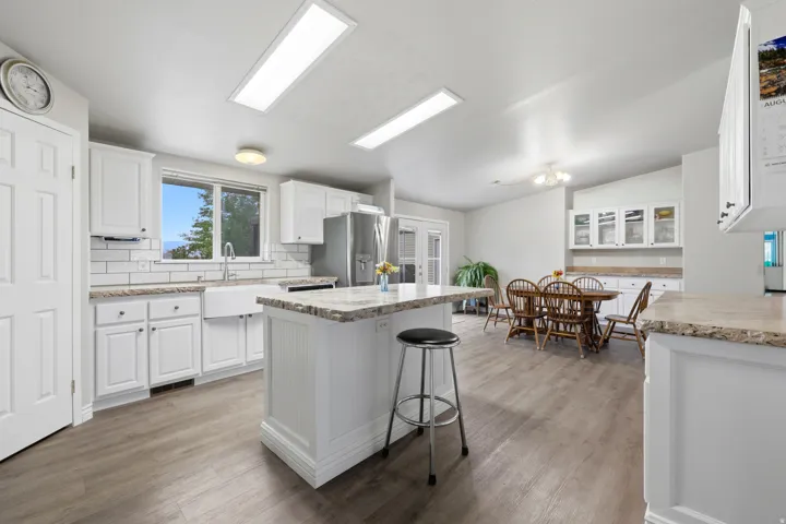 Open concept kitchen featuring white cabinetry, wood-finish flooring, a farmhouse sink, and a center island with a built-in breakfast bar
