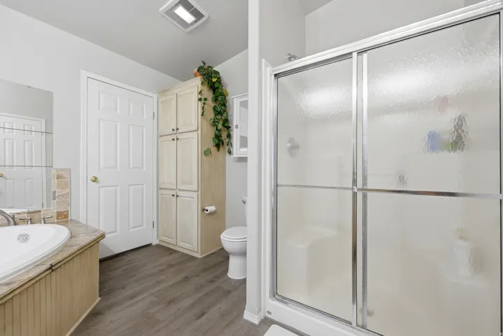 Bathroom featuring a shower with sliding textured glass doors, a vanity with an oval undermount sink, a built-in storage cabinet, and wood-finish flooring