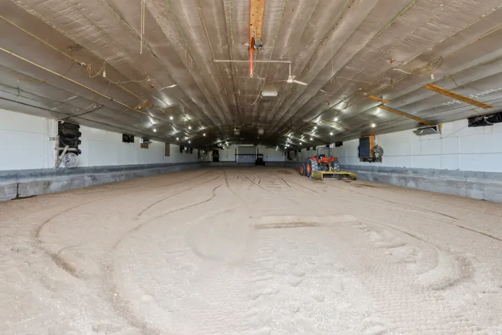 Expansive indoor arena with high ceilings, recessed lighting, ceiling fans, and a wide dirt surface