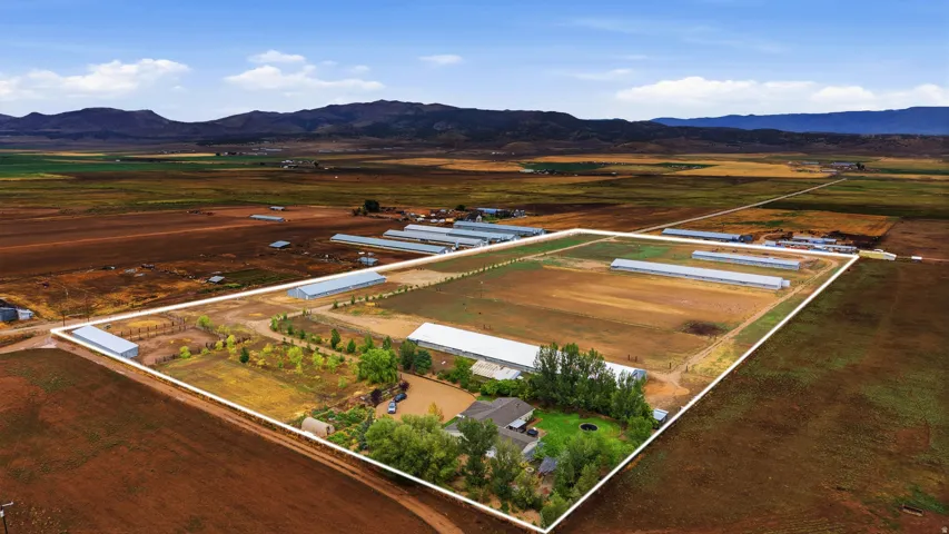 Expansive property featuring multiple large agricultural buildings, a residential structure, and extensive open land