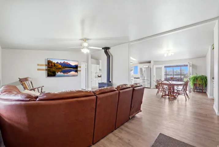 Open-concept living area featuring wood-finish flooring, a ceiling fan, and a built-in wood-burning stove