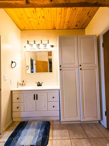 Wood-plank ceiling, vanity with integrated sink, white cabinetry, dark-finish hardware, and tiled flooring