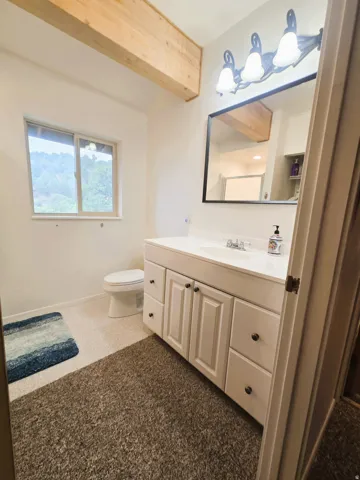 Exposed wood beam, white vanity with ample storage, integrated sink, wall-mounted light fixture, and window