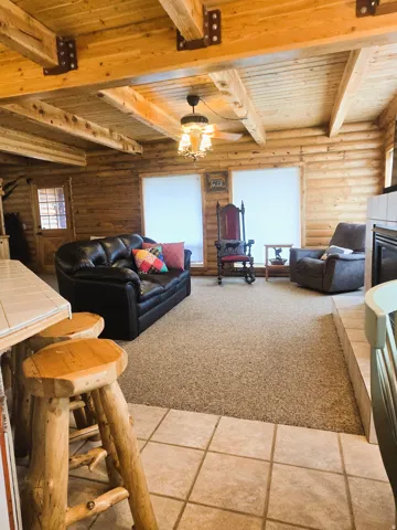 Exposed wood beam ceiling, wood plank walls, tile flooring, carpeted living area, and a built-in fireplace
