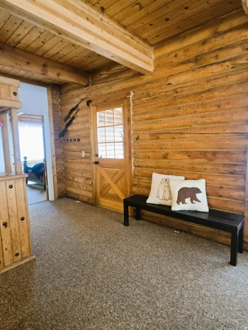 Log wall construction, wood-paneled ceiling, exposed wood beams, and a wood entry door with glass panels