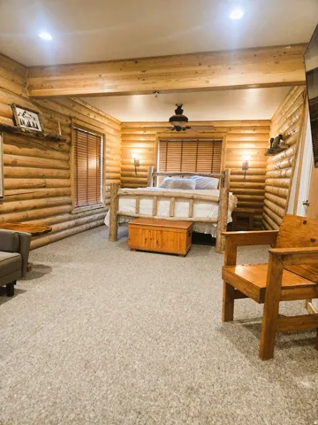 Log-style wood walls, recessed ceiling lighting, light-colored carpeting, ceiling fan, and sconce lighting fixtures