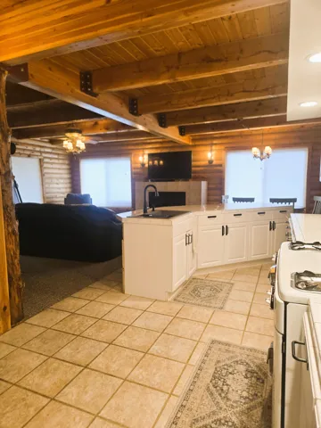 Exposed wood beam ceiling, wood plank walls, white cabinetry with dark hardware, kitchen island with integrated sink, and tile flooring