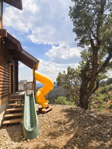 Log cabin exterior with a wood deck, built-in outdoor grill, and a spiral slide