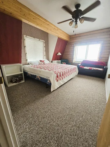 Carpeted flooring, wood beam, ceiling fan with light kit, and natural light from multiple windows