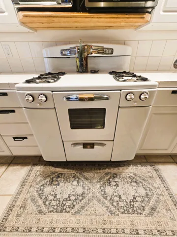 Freestanding gas range with four burners and an integrated oven, set against a white tiled backsplash
