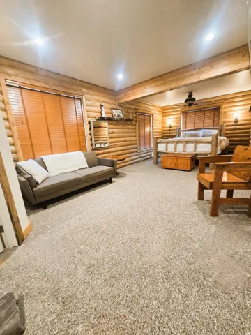 Log-style walls, exposed wood beams, recessed lighting, wall-mounted sconces, and wood-finish window blinds
