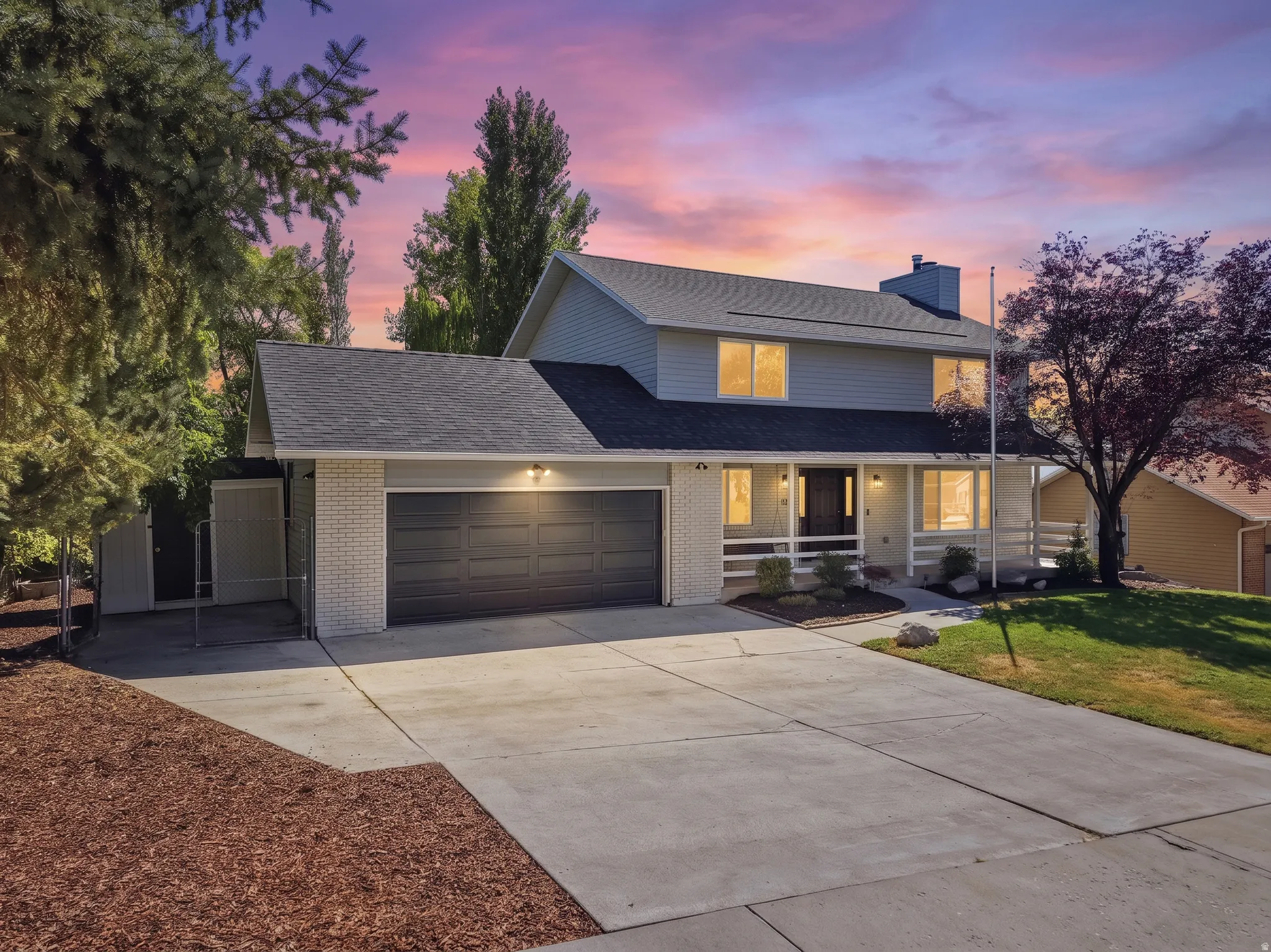 Two-story residence featuring light gray siding, a dark gray shingle roof, a two-car garage with a dark gray door, and light brick accents