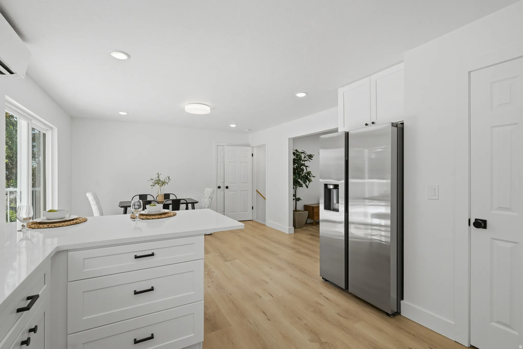 Kitchen island with white cabinetry and dark hardware, stainless steel refrigerator, light wood-finish flooring, recessed lighting, and a pantry