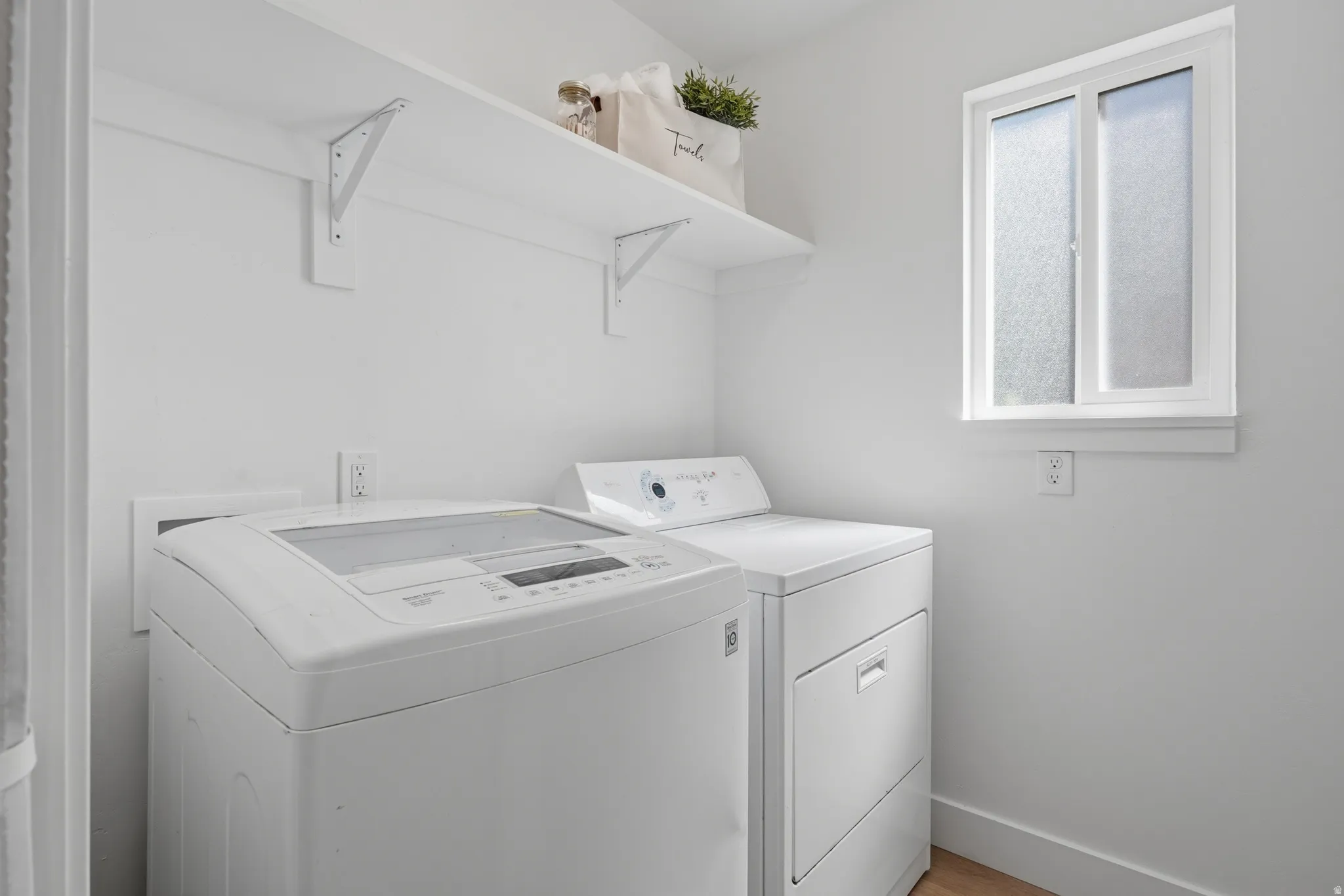 Laundry area with white walls, wood-finish LVP flooring, and a frosted window