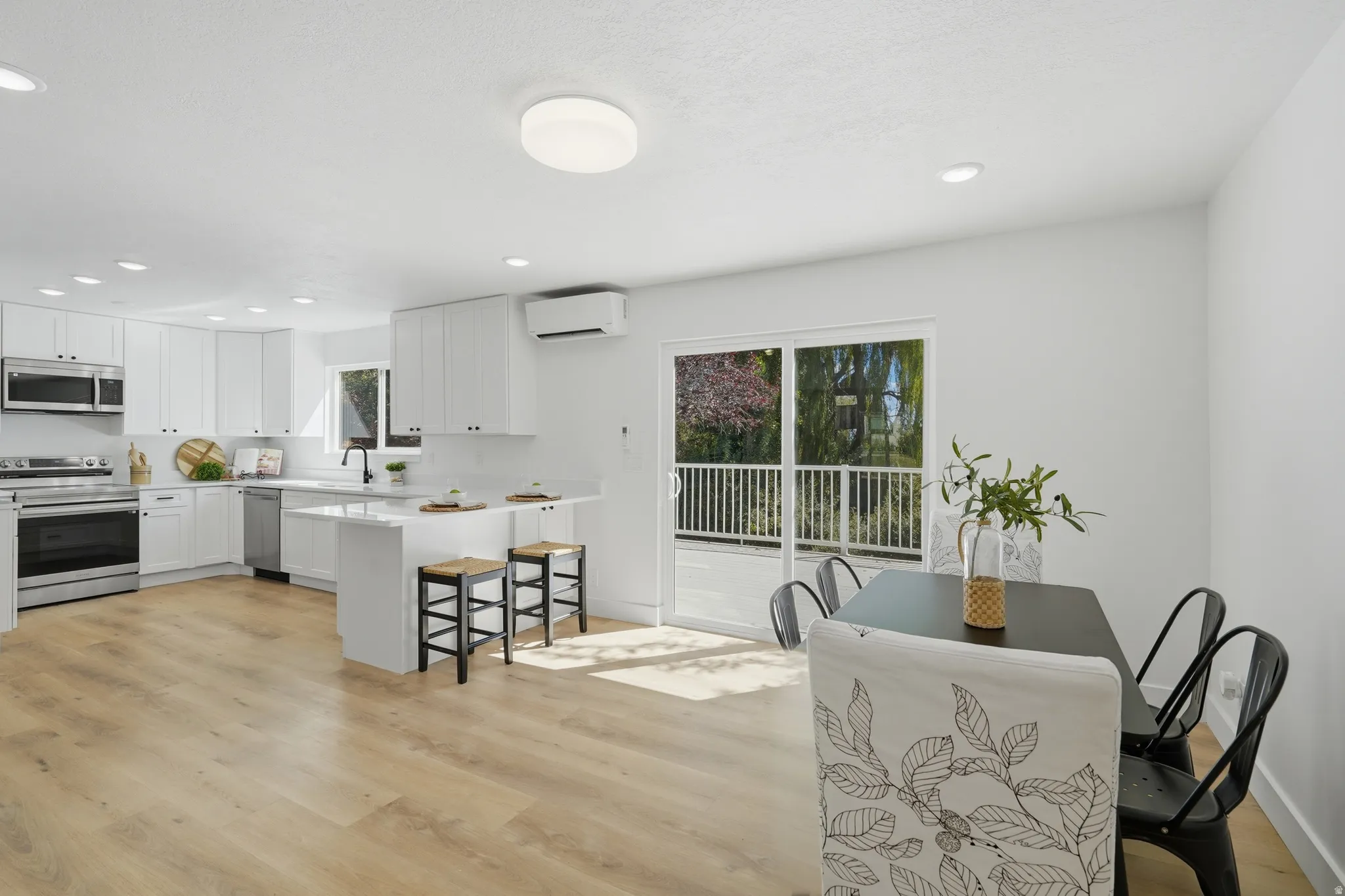 Contemporary kitchen featuring white cabinetry, stainless steel appliances, a center island with bar seating, wood-finish LVP flooring, and a sliding glass door to a deck
