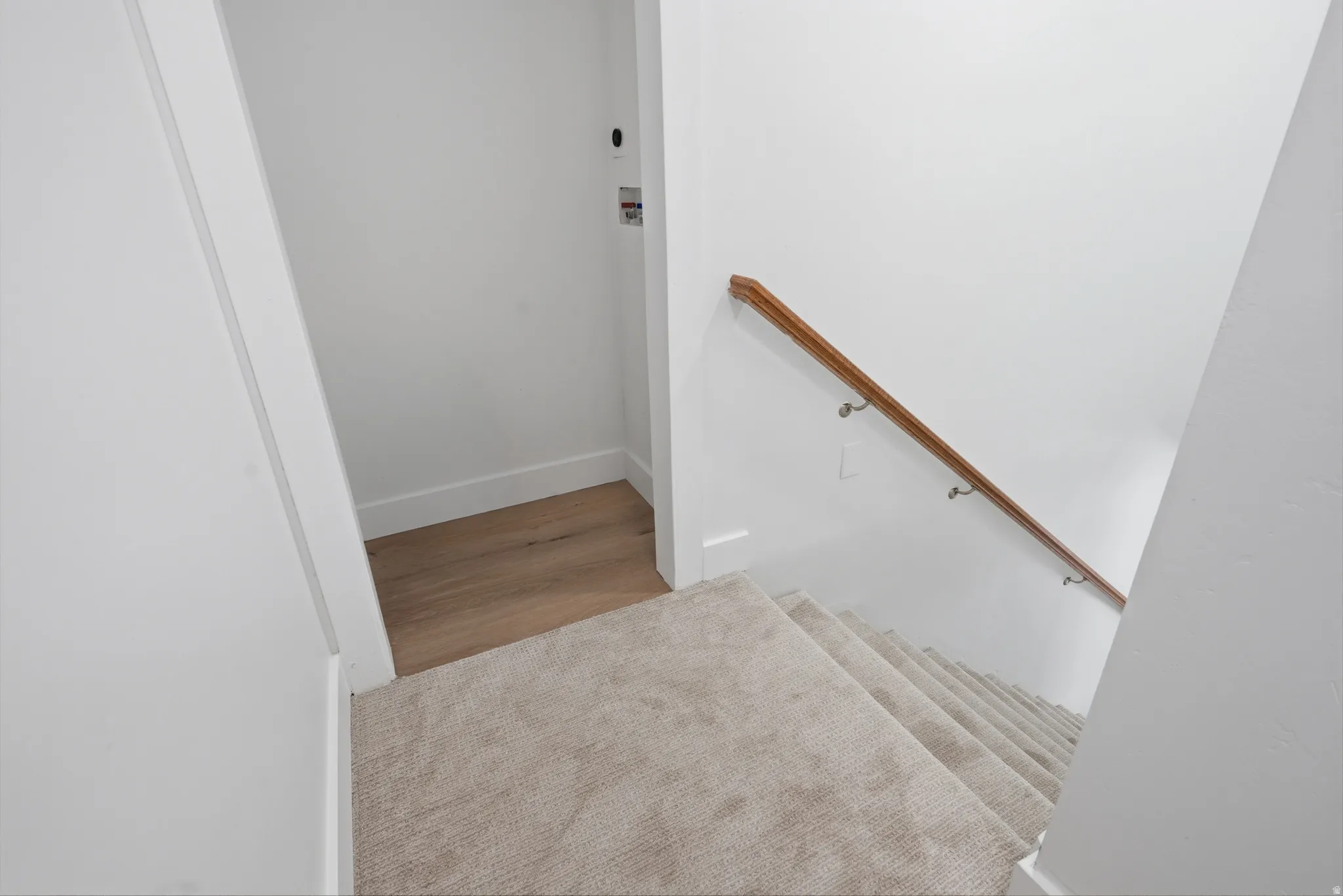 Carpeted staircase with a wood handrail, with a laundry closet for stackable system