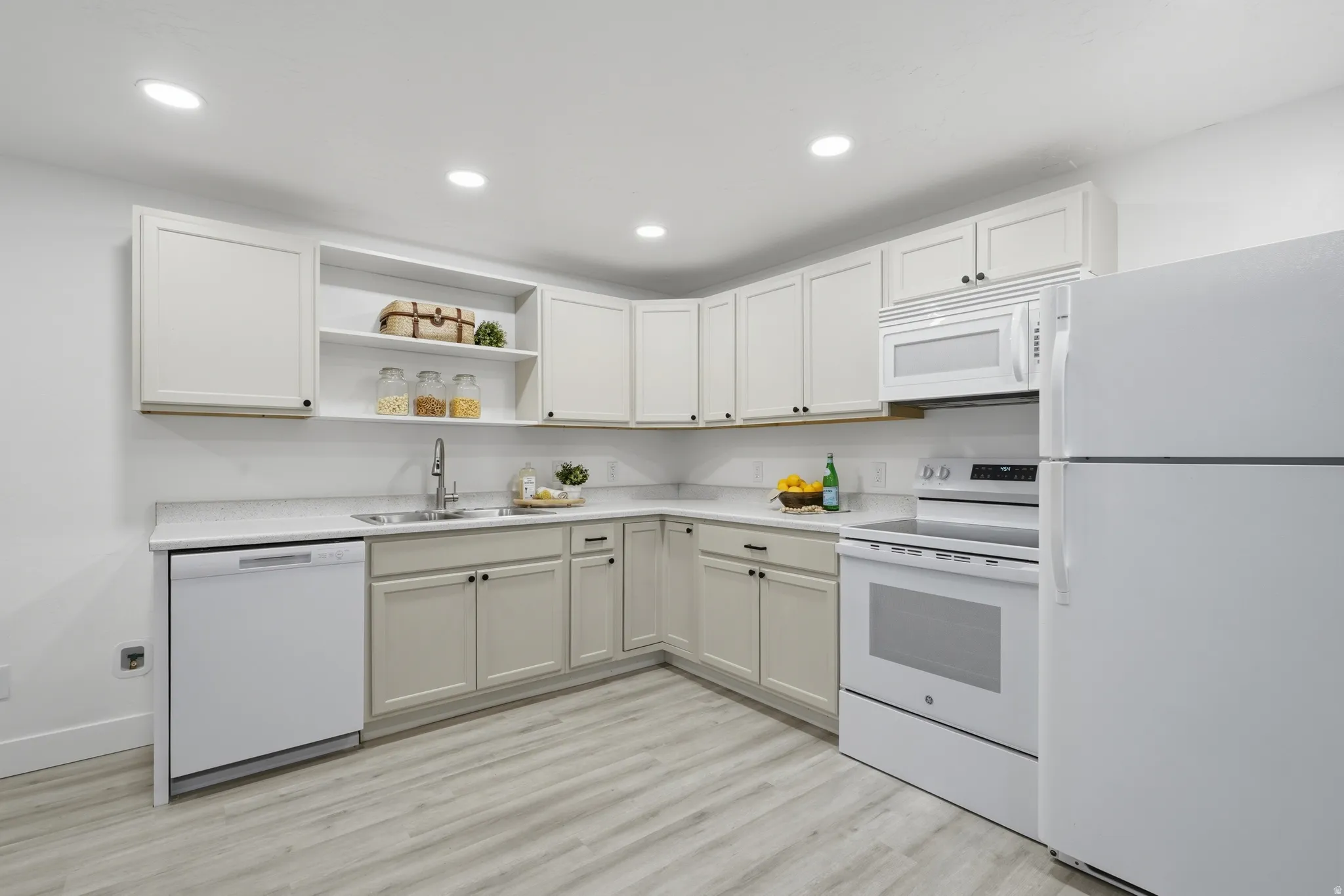 ADU kitchen with recessed lighting, wood-finish laminate flooring, light cabinetry, integrated stainless steel sink, and white appliances