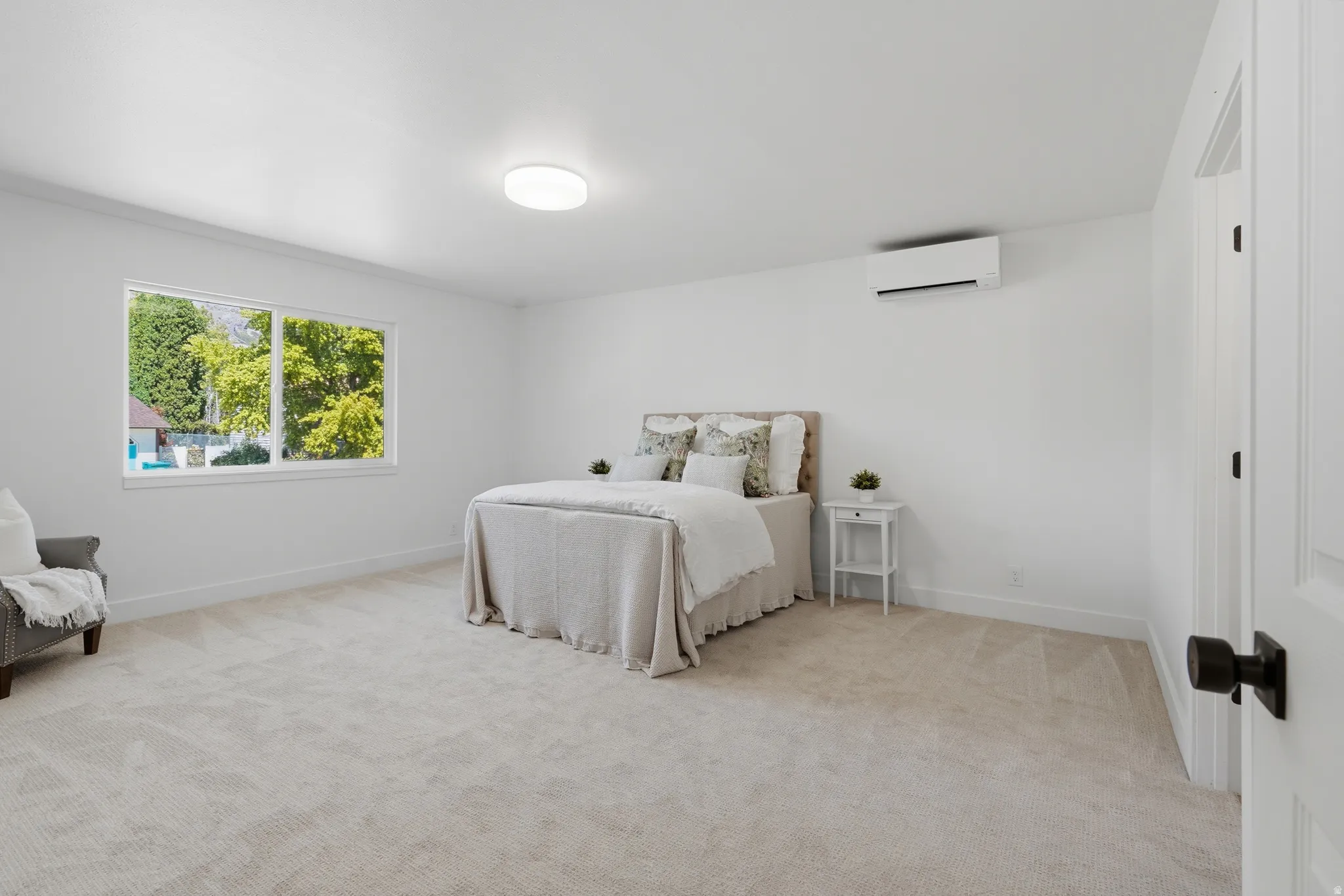 Primary bedroom with neutral carpeting, large windows, recessed lighting, and a wall-mounted climate control unit