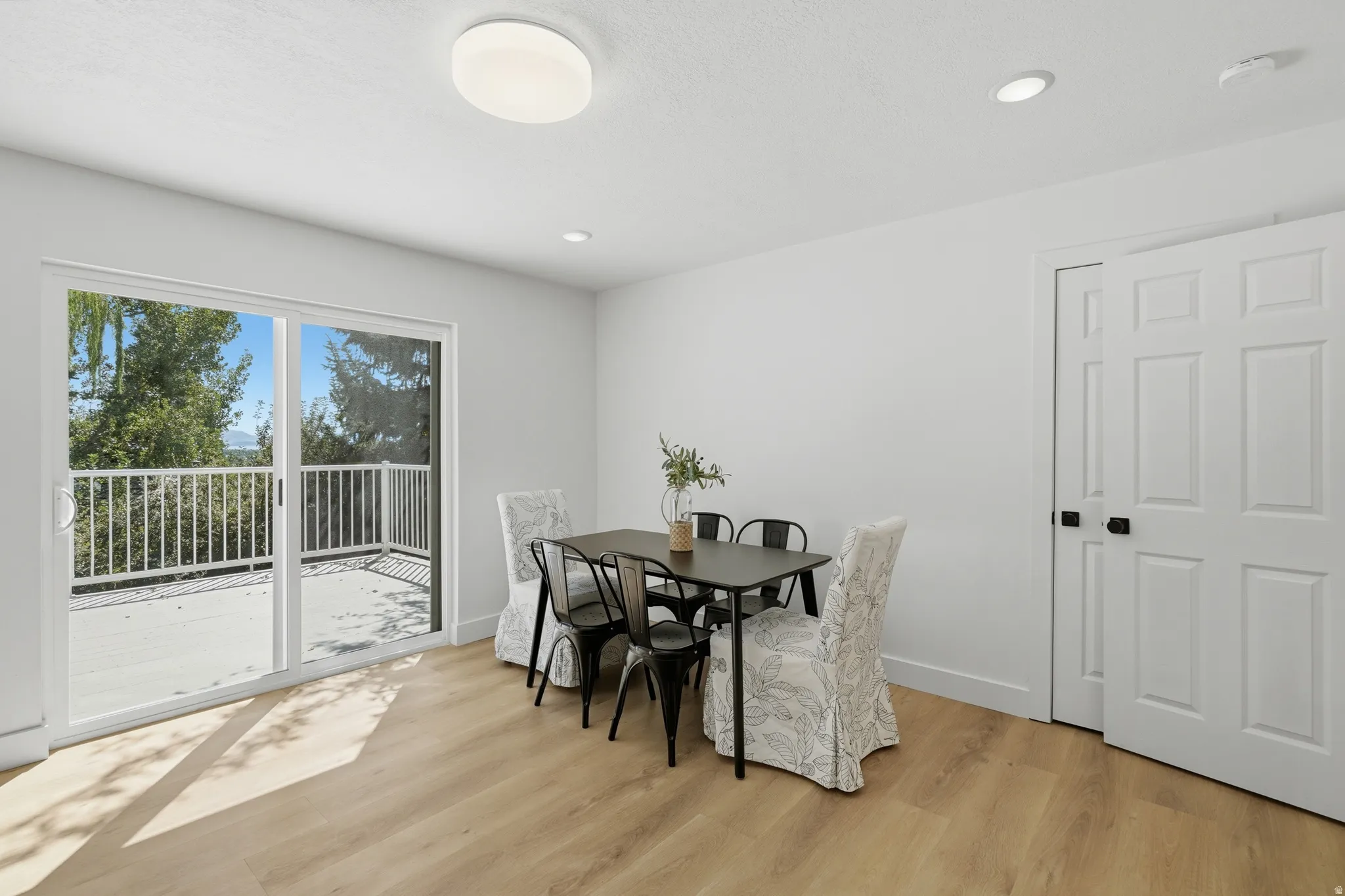 Light wood-finish LVP flooring, white walls, and a sliding glass door leading to an outdoor deck with valley views