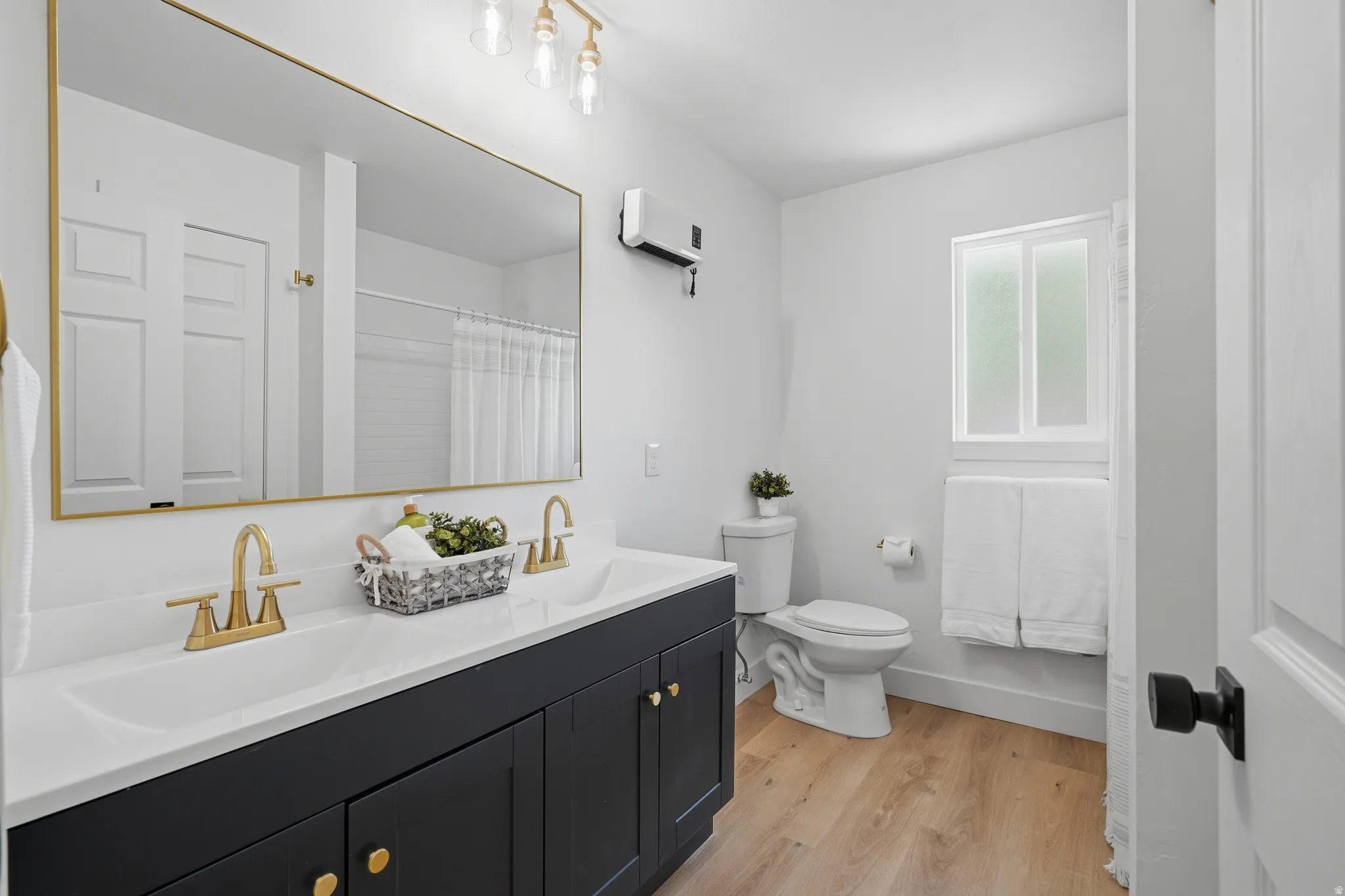 Dual basin vanity with gold-tone hardware, wood-finish LVP flooring, and a privacy window