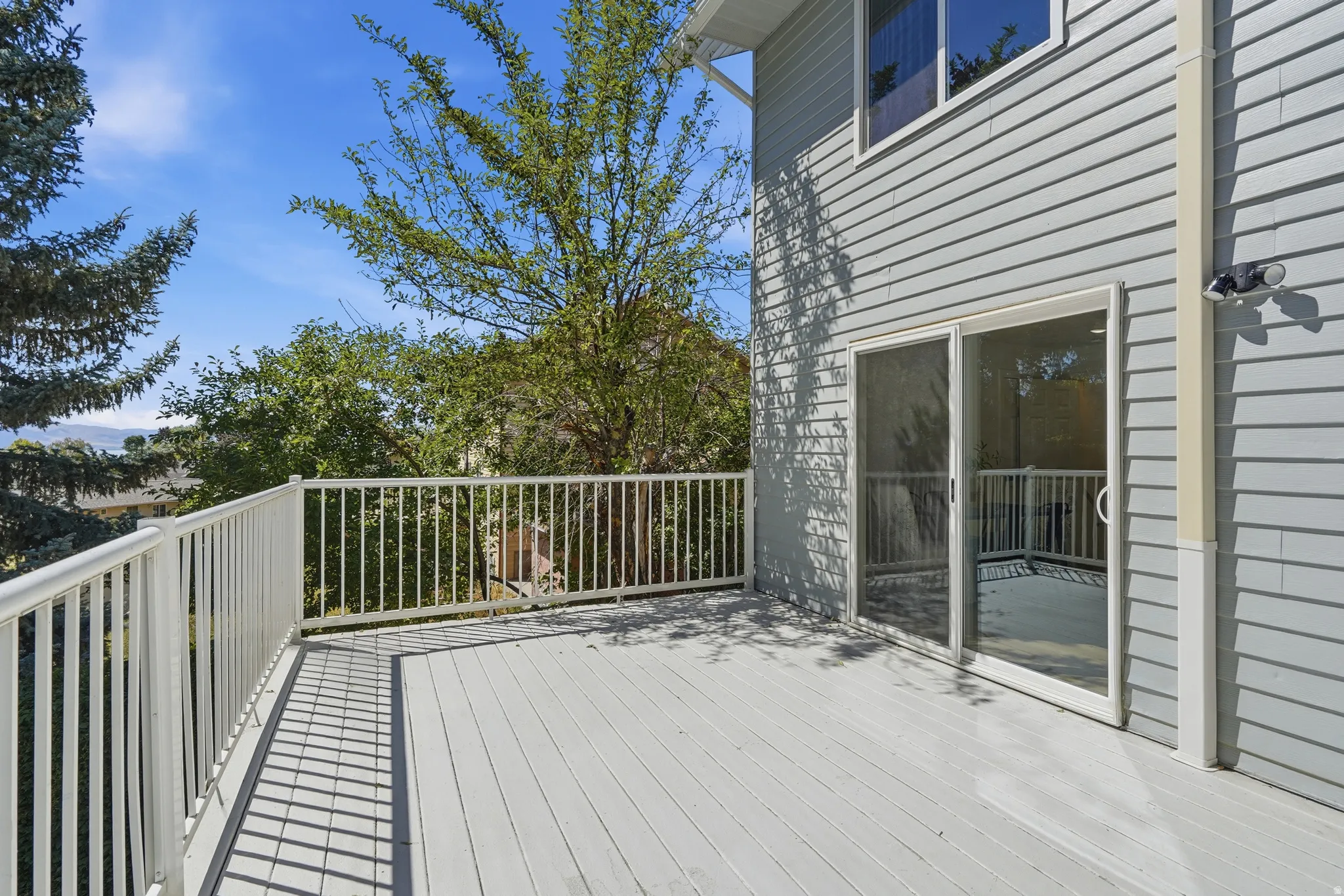 Expansive outdoor deck with white railing, light gray decking, and sliding glass door access to the interior