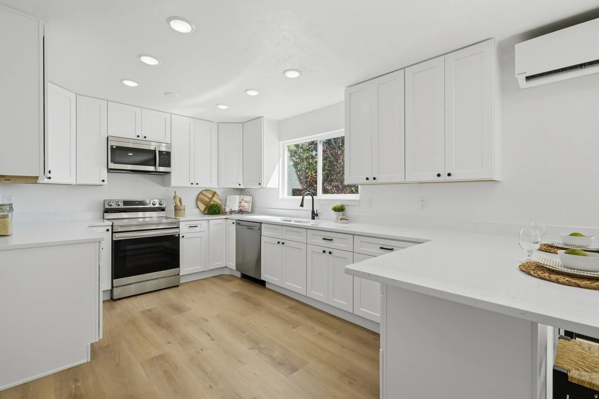 Modern kitchen featuring white cabinetry, stainless steel appliances, light-toned wood-type LVP flooring, recessed lighting, and a window with natural light