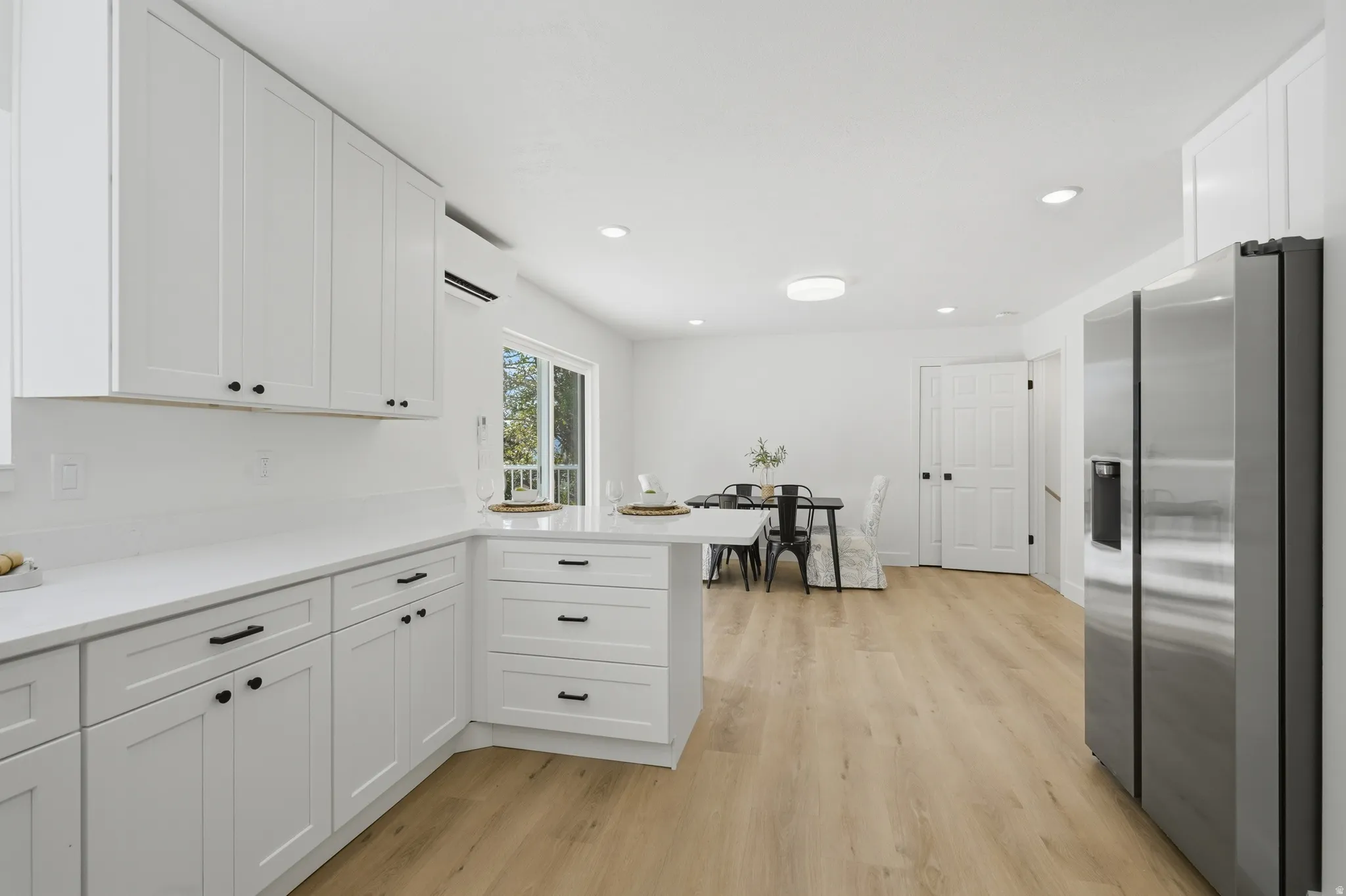 White shaker cabinetry, light wood-finish LVP flooring, stainless steel French door refrigerator, white quartz countertops, and a sliding glass door