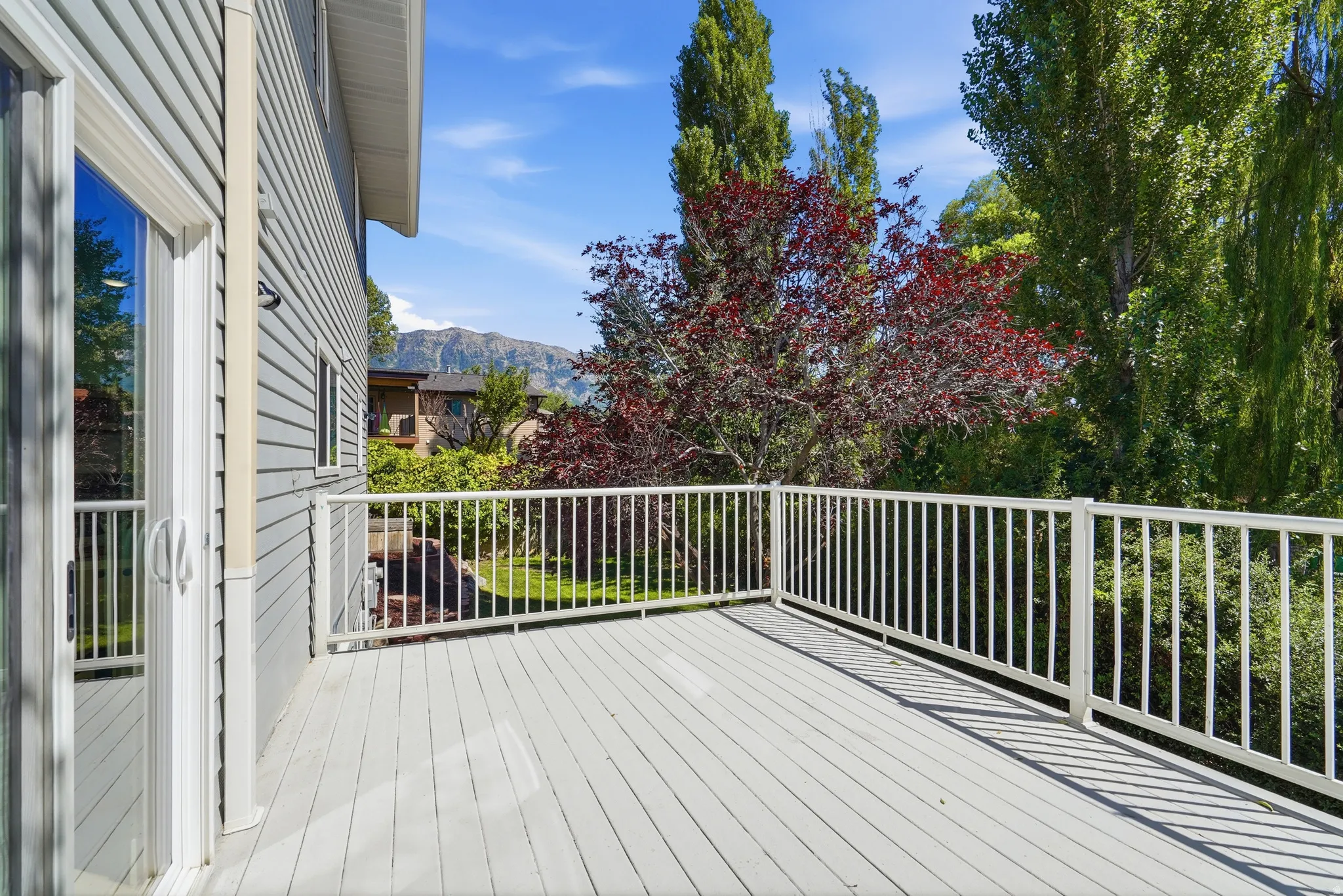 Outdoor decking with white railing, sliding glass door access, and mountain backdrop